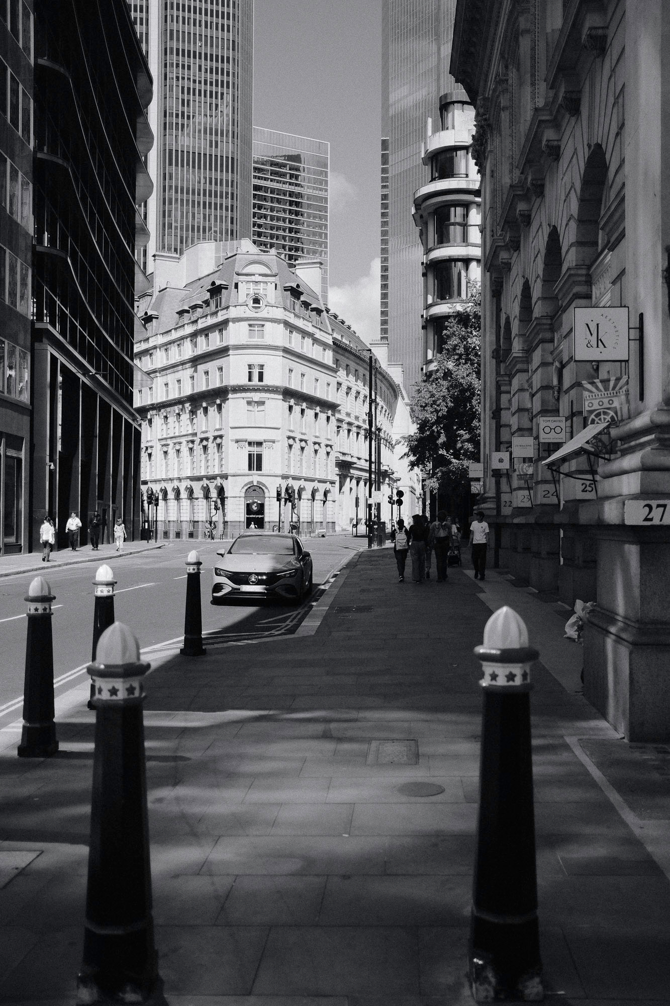 Threadneedle Street in London with a car and people walking on the right side of the road, grayscale